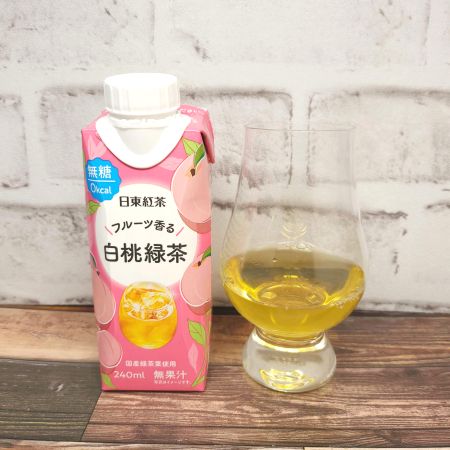 「日東紅茶 フルーツ香る白桃緑茶」とテイスティンググラスの画像